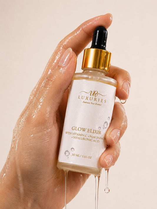 Hand holding a bottle of 'Luxuries' Glow Elixir with droplets on a beige background
